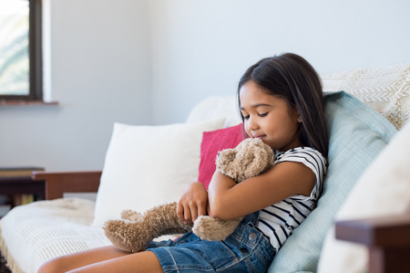 smiling young girl sitting on couch and embracing her teddy bear.
