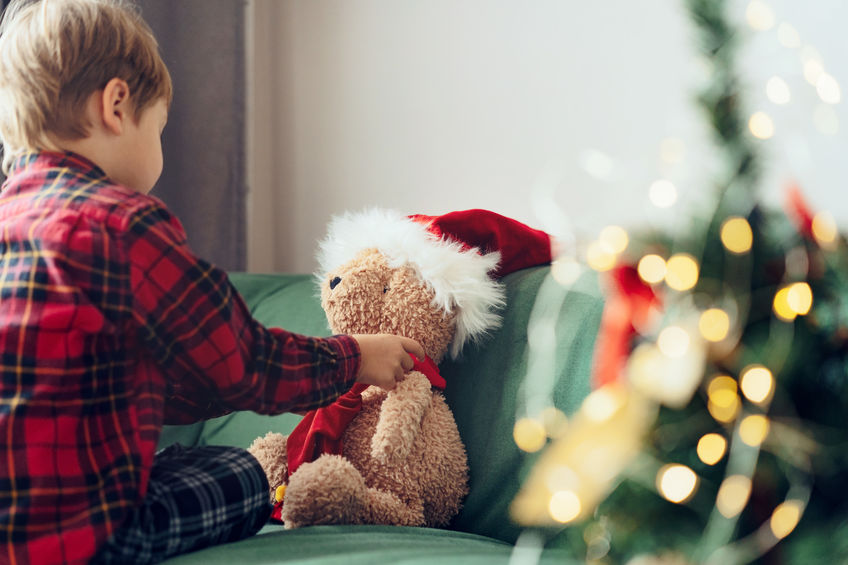 little boy dressing up teddy bear putting on Santa hat. Christmas time.
