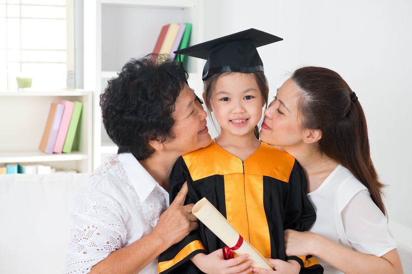 grandparent and parent kissing grandchild on her kinder graduate day.